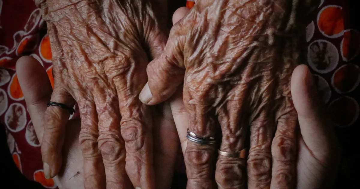 An elderly person's hands with a wedding ring, gently held by a loved one — survivor's pension in Romania: conditions and documents