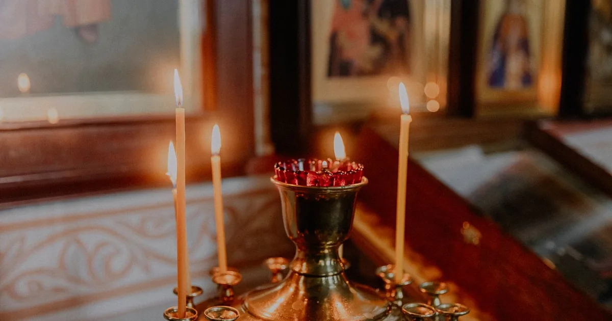 Lumânări de ceară aprinse în fața icoanelor într-o biserică ortodoxă — parastasul de 40 de zile